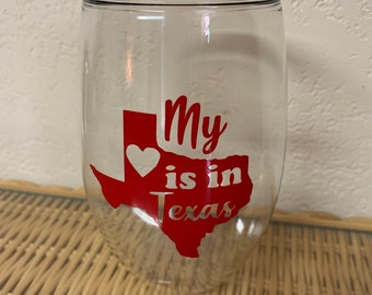 May include: A clear glass wine glass with a red outline of the state of Texas and the text "My heart is in Texas" with a white heart in the center of the state.