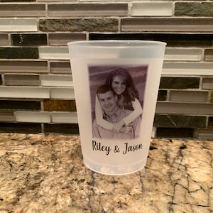 May include: A white plastic cup with a black and white photo of a couple printed on it. The text "Riley & Jason" is printed below the photo.
