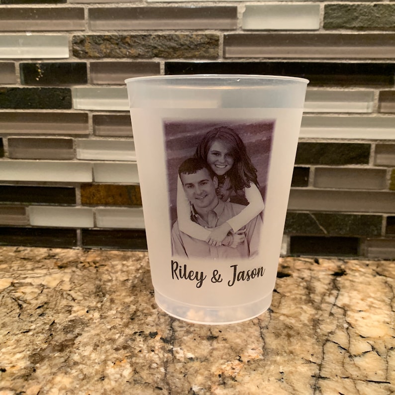 May include: A white plastic cup with a black and white photo of a couple printed on it. The text "Riley & Jason" is printed below the photo.