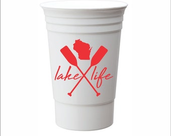 May include: White plastic cup with a red graphic of the state of Wisconsin and two crossed paddles. The text "lake life" is written in red cursive below the paddles.