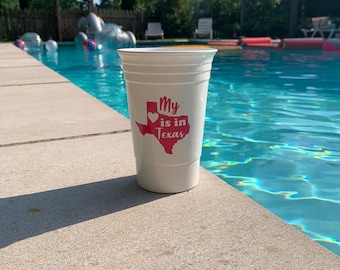May include: White plastic cup with a red heart and the text "My heart is in Texas" printed on it. The cup is sitting on the edge of a swimming pool.