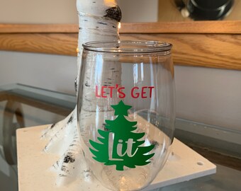 May include: Clear plastic wine glass with a green Christmas tree and the text "Let's Get Lit" in red.