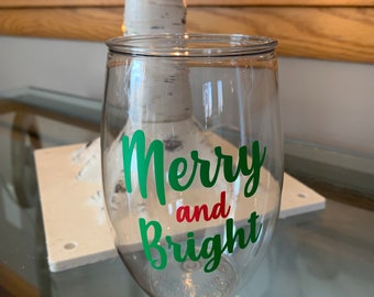 May include: Clear glass wine glass with a green and red vinyl decal that says "Merry and Bright".