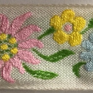 Cinta de jacquard tejida con diseño floral vintage, flores de edelweiss rosas, amarillas, celestes y verdes sobre un fondo blanco de 2,5 cm.