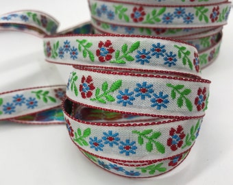 May include: White ribbon with a red, blue, and green floral pattern. The ribbon is woven with a repeating design of flowers and leaves.