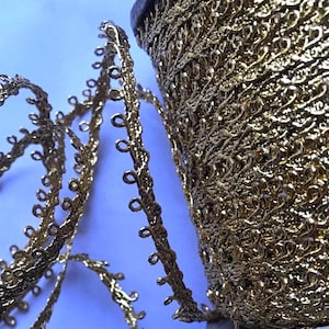 May include: Gold metallic trim with a delicate, intricate design. The trim has a scalloped edge with small loops along the edge.
