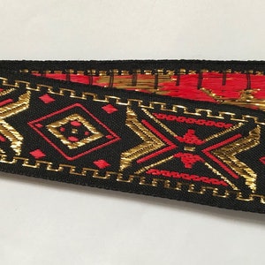 May include: Black ribbon trim with a geometric pattern in red and gold. The pattern features diamonds and zigzags.