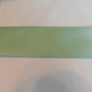 May include: A light green satin ribbon with a smooth, silky texture.