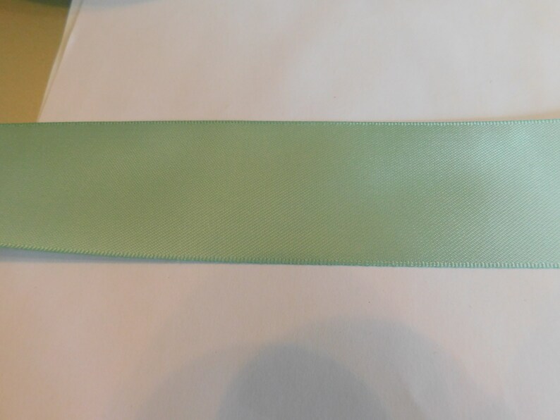 May include: A light green satin ribbon with a smooth, silky texture.