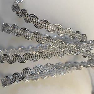 Peut inclure: Garniture métallique argentée avec un motif ondulé et festonné. Cette garniture est idéale pour ajouter une touche d'élégance à tout projet.