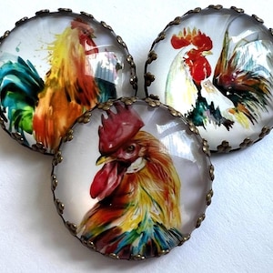May include: Three round glass cabochons with rooster illustrations. Each features a colorful rooster design with red, yellow, orange, and blue hues. The cabochons are set in antique bronze-colored metal frames.