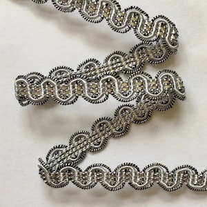 May include: Silver and black decorative trim with a scalloped edge. The trim is made of a woven fabric with a metallic sheen.