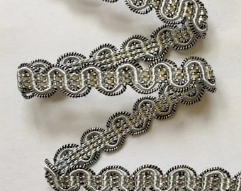 May include: Silver and black decorative trim with a scalloped edge. The trim is made of a woven fabric with a metallic sheen.