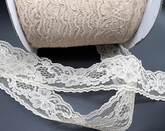 May include: A roll of ivory lace trim with a delicate floral pattern. The lace is shown unrolled, revealing the intricate design.