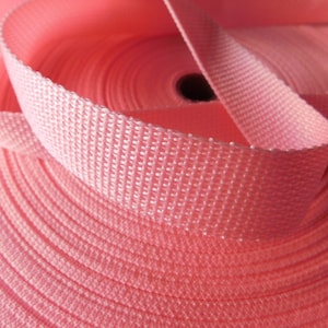 May include: A close-up of a pink woven webbing roll. The webbing is tightly wound and has a textured surface.