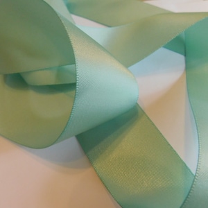 May include: A roll of light green satin ribbon. The ribbon is folded and twisted, showing its smooth, silky texture.