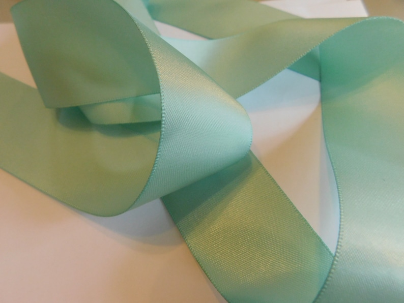 May include: A roll of light green satin ribbon. The ribbon is folded and twisted, showing its smooth, silky texture.