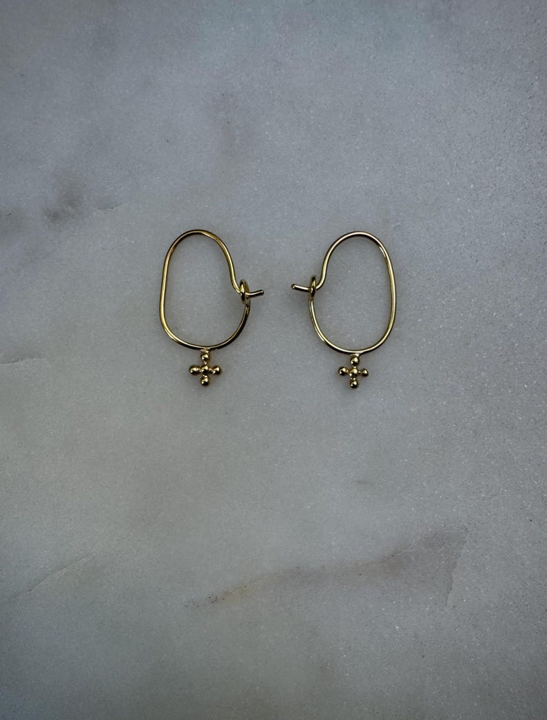 May include: A pair of gold hoop earrings with a small, textured cross charm hanging from each hoop.