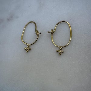 May include: A pair of gold hoop earrings with a small, textured cross charm hanging from each hoop.