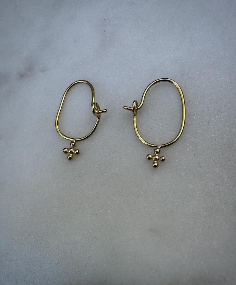 May include: A pair of gold hoop earrings with a small, textured cross charm hanging from each hoop.