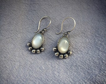 May include: A pair of silver earrings with a white oval gemstone and a silver bead fringe.