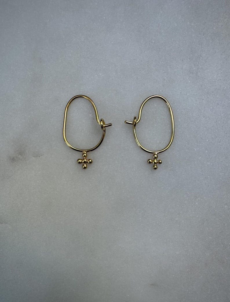 May include: A pair of gold hoop earrings with a small cross charm hanging from each hoop.