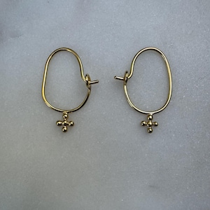 May include: A pair of gold hoop earrings with a small cross charm hanging from each hoop.