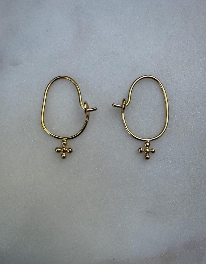 May include: A pair of gold hoop earrings with a small cross charm hanging from each hoop.