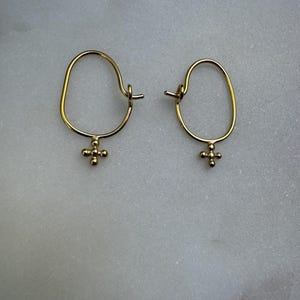May include: A pair of gold hoop earrings with a small cross charm hanging from each hoop.