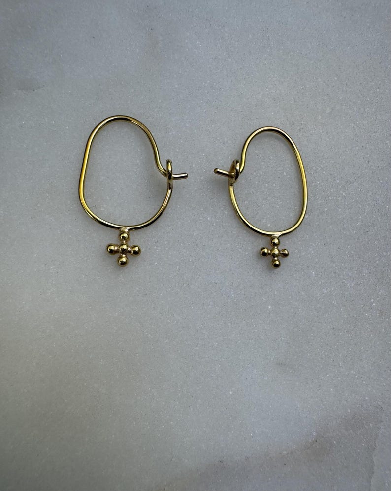 May include: A pair of gold hoop earrings with a small cross charm hanging from each hoop.