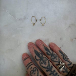 May include: A pair of gold hoop earrings with a small, textured charm hanging from each hoop.