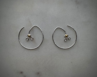 May include: A pair of silver hoop earrings with a small gold bead accent on each hoop.