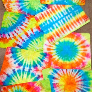 May include: A set of eight tie-dye fabric squares in various colors, including blue, green, yellow, orange, and pink. The squares are arranged in a random pattern on a brown surface.