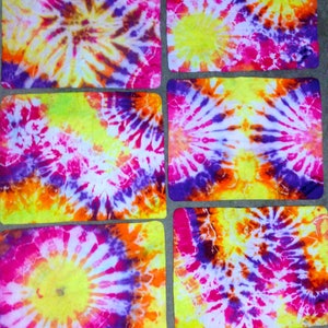 May include: Set of six tie-dye coasters in shades of yellow, pink, purple, and orange. The coasters are made of fabric and have a circular pattern.