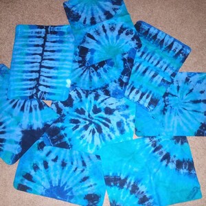 May include: A set of nine blue and black tie-dye fabric squares. The squares are arranged in a random pattern on a brown surface.