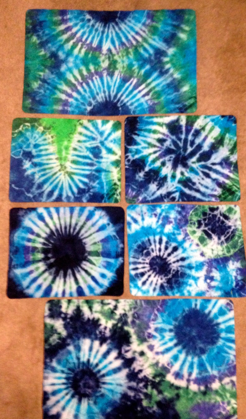 May include: Five square tie-dye fabric coasters in shades of blue, green, and white. The coasters feature a circular pattern with a dark blue center.