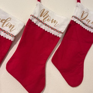May include: Four red Christmas stockings with white felt cuffs and gold glitter lettering. The stockings are labeled "Mom", "Dad", and "Eden".