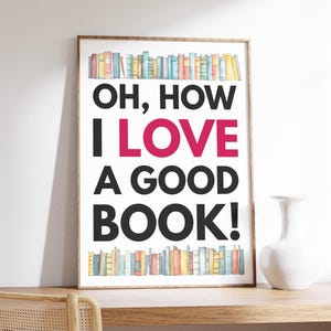 Puede incluir: Un póster blanco con un marco negro y una ilustración de acuarela de una estantería llena de libros coloridos. El póster tiene el texto "OH, HOW I LOVE A GOOD BOOK!" en letras negras y rosas.