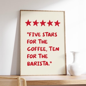 Op de afbeelding: Een ingelijst print met een witte achtergrond en rode tekst. De tekst luidt "Vijf sterren voor de koffie, tien voor de barista". Boven de tekst staan vijf rode sterren.