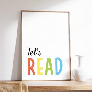 May include: A framed print with the text "let's READ" in colorful letters. The letters are red, yellow, green, and blue. The print is on a white background and has a wooden frame.