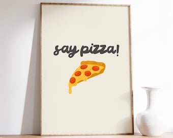 May include: A beige printable wall art print with the text "say pizza!" in black script font and a cartoon image of a slice of pizza with red pepperoni and melted cheese.