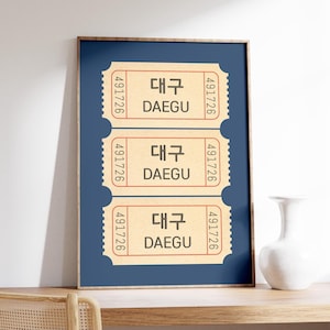 May include: A framed print featuring three vintage-style tickets. Each ticket is beige with the city name "DAEGU" in both Korean and English, along with the number "491726". The background is a dark blue.