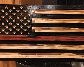 Puede incluir: Una bandera americana de madera con un esquema de colores rojo, blanco y azul. La bandera está hecha de tablones de madera individuales y tiene un aspecto desgastado. Las estrellas están talladas en la madera.