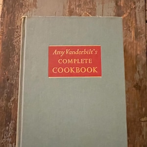 May include: A teal blue hardcover cookbook with a red spine and the title "Amy Vanderbilt's Complete Cookbook" in gold lettering.