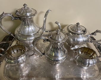 May include: A silver tea set with a teapot, creamer, sugar bowl, and a tray. The set is ornate and features a fluted design.