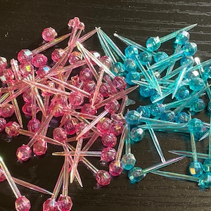 May include: A large pile of iridescent pink and blue plastic Christmas tree light bulbs with a pointed end. The bulbs are arranged in a random pattern.