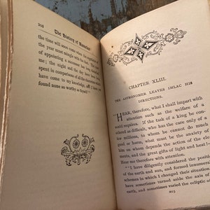 May include: An open book with yellowed pages and a decorative design on the cover. The book is titled "The History of Rasselas" and the chapter is titled "The Astronomer Leaves Imlac His Directions". The text on the page discusses the responsibilities of a ruler and the importance of considering the welfare of the people.
