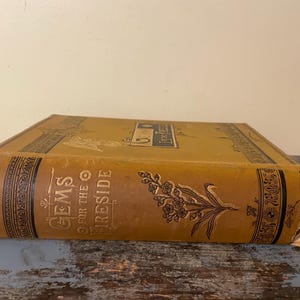 May include: A vintage book titled "Gems for the Fireside" with a gold and black cover and a floral design. The book is in good condition with some wear and tear.