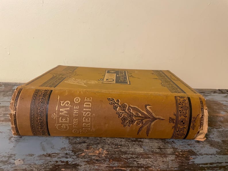 May include: A vintage book titled "Gems for the Fireside" with a gold and black cover and a floral design. The book is in good condition with some wear and tear.