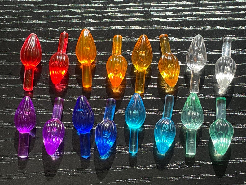 May include: Assortment of 18 clear plastic Christmas tree light bulb covers in various colors, including red, orange, yellow, green, blue, purple, and clear. The bulbs are arranged in rows on a black surface.